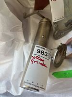 Photo of pewter coffee grinder showing cylindrical shape, hand crank, and manufacturer's label.