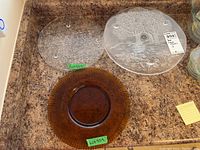 Two round cheese plates: one clear with engraving of a tree and landscape, one amber with ribbed texture.