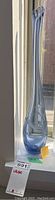 Full view of the tall blue-gray hand blown glass vase showing slender neck and bulbous base, standing on window sill with natural light highlighting the glass finish.