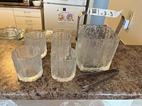 Full set of Hoya crystal ice bucket, four matching glasses, and stainless steel tongs on kitchen counter.