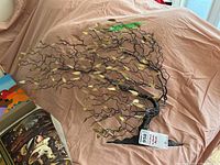 Full view of metal tree wall art sculpture showing twisted black metal branches and gold leaves on a pink fabric background with a sale tag