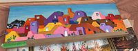 Full view of oil painting depicting colorful adobe buildings on stretched canvas with wood frame.