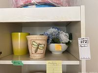 Three planters and faux flower bouquet placed on a white shelf with visible lot tag.