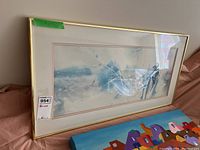 Framed abstract print featuring blue and white floral or botanical elements, matted and behind glass in gold frame.