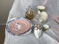 Royal Doulton swan figure decorated with colorful china flowers, pink Royal Doulton and blue bordered plates, golden glass angel figurine, porcelain creamer, and Spode cup.