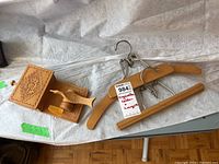 Three items displayed on a table: a carved wooden cigarette holder and two wooden hangers with metal hooks and clips.