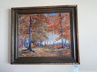 Front view of the framed painting showing a colorful forest with trees, leaves, and a path. Frame is dark wood with ornate details and some damage visible on the corners.