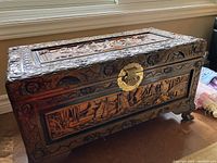 Full view of rectangular wooden chest with carved details and brass closure on front.