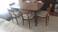 Six teak chairs arranged around a dining table on a rug.