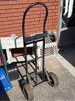 Front angle of dolly showing handle, two large rear wheels, one small front wheel on right side, and missing left front wheel.