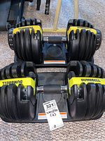 Pair of adjustable dumbbells in plastic storage trays on carpeted floor