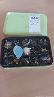 Closed box with multiple compartments holding various costume jewelry earrings, showing some earrings visible inside.