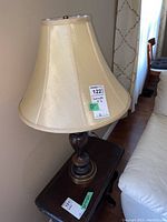 Photo showing one of the matching table lamps with beige fabric shade and dark wood carved base, standing on a dark table next to sofa.
