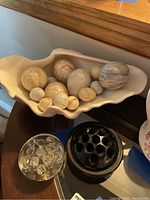 Overall lot showing marble eggs in shell-shaped porcelain bowl, and both glass flower frogs on surface nearby.