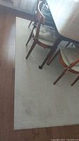 View of beige area rug under dining table with chairs showing geometric rectangular pattern.