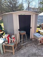 Front view of metal storage shed with open sliding doors, showing interior and immediate surrounding items such as a stool and decorative dog statues on a small table.