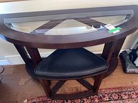 Front view of half-moon wood console table with beveled glass inset top and matching stool tucked beneath.