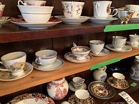 Display of multiple teacups and saucers on wooden shelves showing variety of floral patterns and cup styles