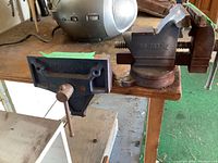 Three vices mounted on a wooden workbench, showing two Mastercraft flat press vices and one traditional metal vice with model number.