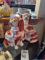 Two red and white ceramic China dog figurines placed side by side on a glass surface, showing their front and side profiles with paint wear visible.