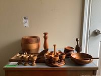Overview of all wooden kitchenware items including egg cups on tray, single egg cups, cheese board, mortar and pestle, coasters, pepper grinder, wooden bowl with lid and spoon.