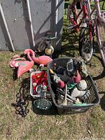 Wide shot showing three pink flamingo lawn ornaments, metal bee sculpture, basket with various garden items, and portions of bicycles in the background.
