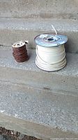 Two partial spools of insulated wire on concrete steps: brown spool at left, white spool at right.