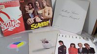 Six classic rock vinyl albums arranged, showing covers of Aerosmith, Slade?, Rolling Stones, Pretenders, and two additional albums with distinctive cover art including a pie chart and a cat in a bowl.