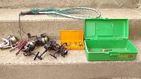 Photo of 6 fishing reels, small fishing net and two tackle boxes placed on concrete step.