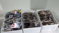 Boxes containing numerous individually packaged new sunglasses in two distinct styles and multiple colors