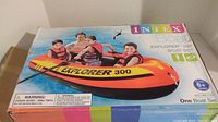 Photo of the Intex Explorer 300 inflatable boat set box showing branding, illustration of the boat with children, and included items like pump and oars.