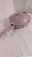 Image showing the purple/lilac ceramic non-stick pan with matching lid, viewed angled to display the pan shape and handle.