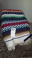 Folded Mexican style woven blanket on a dark surface showing multicolored horizontal stripes with fringe tassels