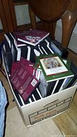 Box filled with books and cases for CDs/DVDs sitting on floor between chairs