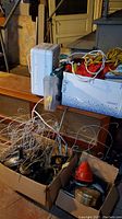 Photo showing Weather Works heater, large white plastic bin with tools or cords inside, cardboard boxes filled with tangled cords and garden tool-like metallic items, basement setting with shelving unit and paint cans in background.