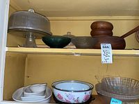 Photo shows a glass cake stand with lid on top shelf, two textured glass bowls in dark green and brown, and three round teak wood bowls with ladle on right side.