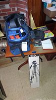 Blue camera bag with Canon A-1 film camera visible inside, several rolls of 35mm film and accessories on a table with photography book, remote or flash, and lens caps.