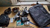 Full overview of all items on table showing Minolta Hi-matic camera with manual and case, digital camera, hotshoe flash, Discman, and Targus laptop bag.