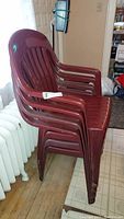 Stacked set of four maroon plastic chairs showing side profile and armrests.