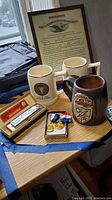 Overview photo showing the harmonica in box, two beer steins, and military medals on a table near window