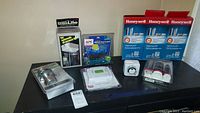 Photo showing all items on table including door knobs, thermostat, surge protector, and three boxes of Honeywell HEPA filters.