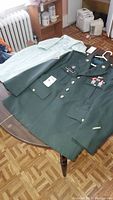 Photo shows green U.S. Army military jacket with pins and a light-colored shirt laid on a table.