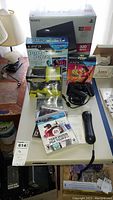 Sony PlayStation 3 console box with 320GB capacity shown on table with multiple loose game cases and controllers visible