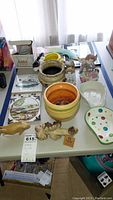Overview of multiple pottery items including planters, figurines, plates, coasters, mug on a table