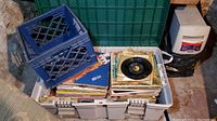 Top view of white plastic bin holding vintage record albums and 45 RPM records in CBS envelopes with a blue milk crate on top.