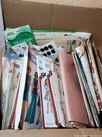 Top-down view of cardboard box containing assorted vintage sewing patterns primarily Simplicity brand, packets of buttons, tailor's chalk, and fabric.