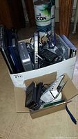 View of box containing laptops, phones, and assorted electronics and accessories including cords and remote controls.