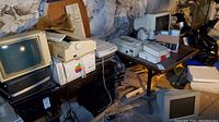 Multiple devices on basement table including boxed LaserWriter, ImageWriter II, keyboard, scanner and CRT monitor