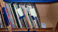 Overhead view of jazz and classical vinyl record albums stored vertically on a shelf with blue painter's tape securing some areas.
