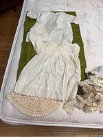Two antique baby dresses with lace laid flat on mattress; vintage lace trims on side